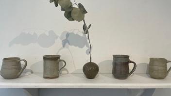narrow shelf display of mugs with a bud vase in the middle